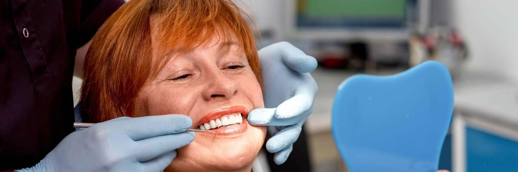Lady looking at her teeth in the mirror after teeth whitening at Edmond Dental Center
