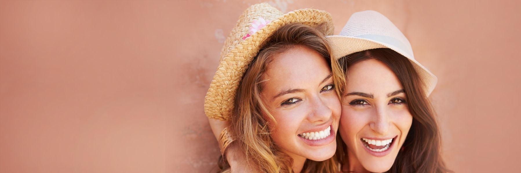 Two women in hats smiling against a wall near Edmond OK